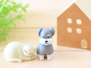 白い猫と灰色の犬のミニチュアフィギュアが家のオブジェと並んでいるイメージ画
