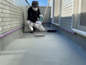 ベランダ床面に防水塗料をローラーで丁寧に塗布する職人